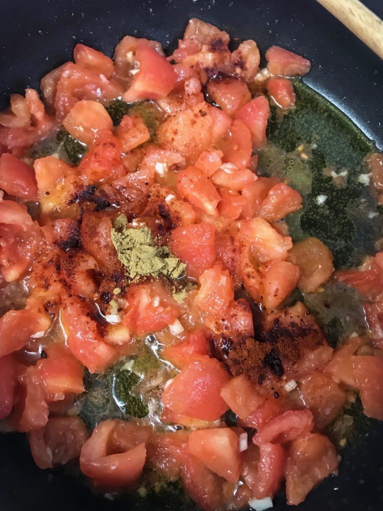 a saute pan with chopped tomatoes, garlic, and cumin and paprika in olive oil 