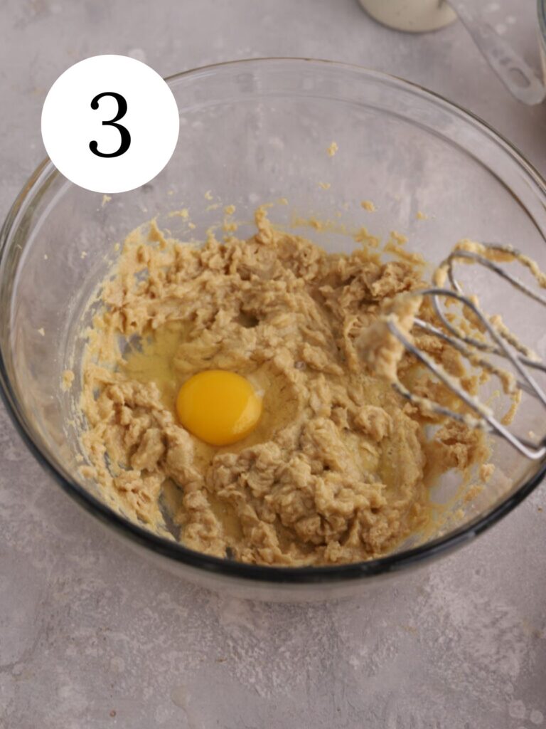 A mixing bowl with an egg being added to batter.