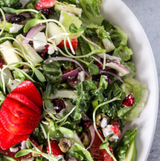 A serving platter full of a colorful salad of romaine lettuce and vegetables with dressing and a strawberry on top