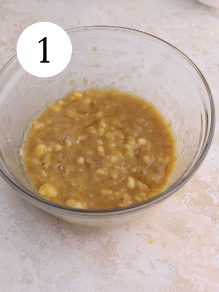 Mashed bananas mixed with sugar in a glass mixing bowl.