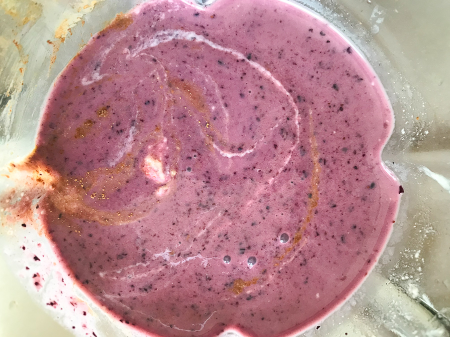 a mixing bowl with a blueberry smoothie inside with traces of cinnamon
