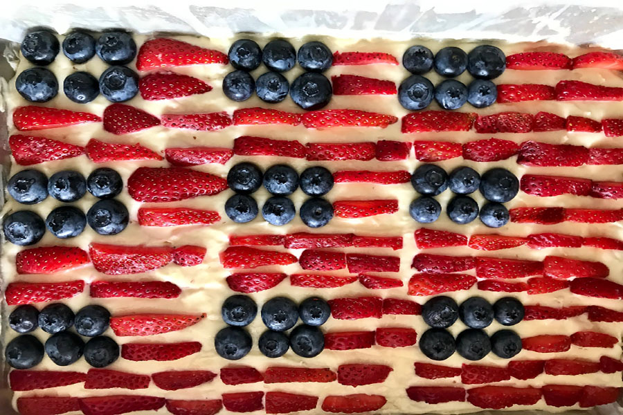 a beautiful american flag cake with blueberries and sliced strawberries on a white cake in a cake pan
