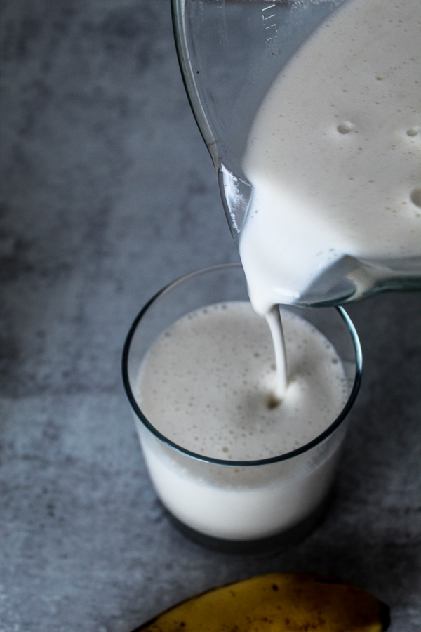 a blender pouring thick, frothy, creamy banana smoothie into a glass 