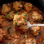 kofta meatballs in a deep saucepan with rich tomato sauce and flecks of chopped parsley and a spoon holding a meatball