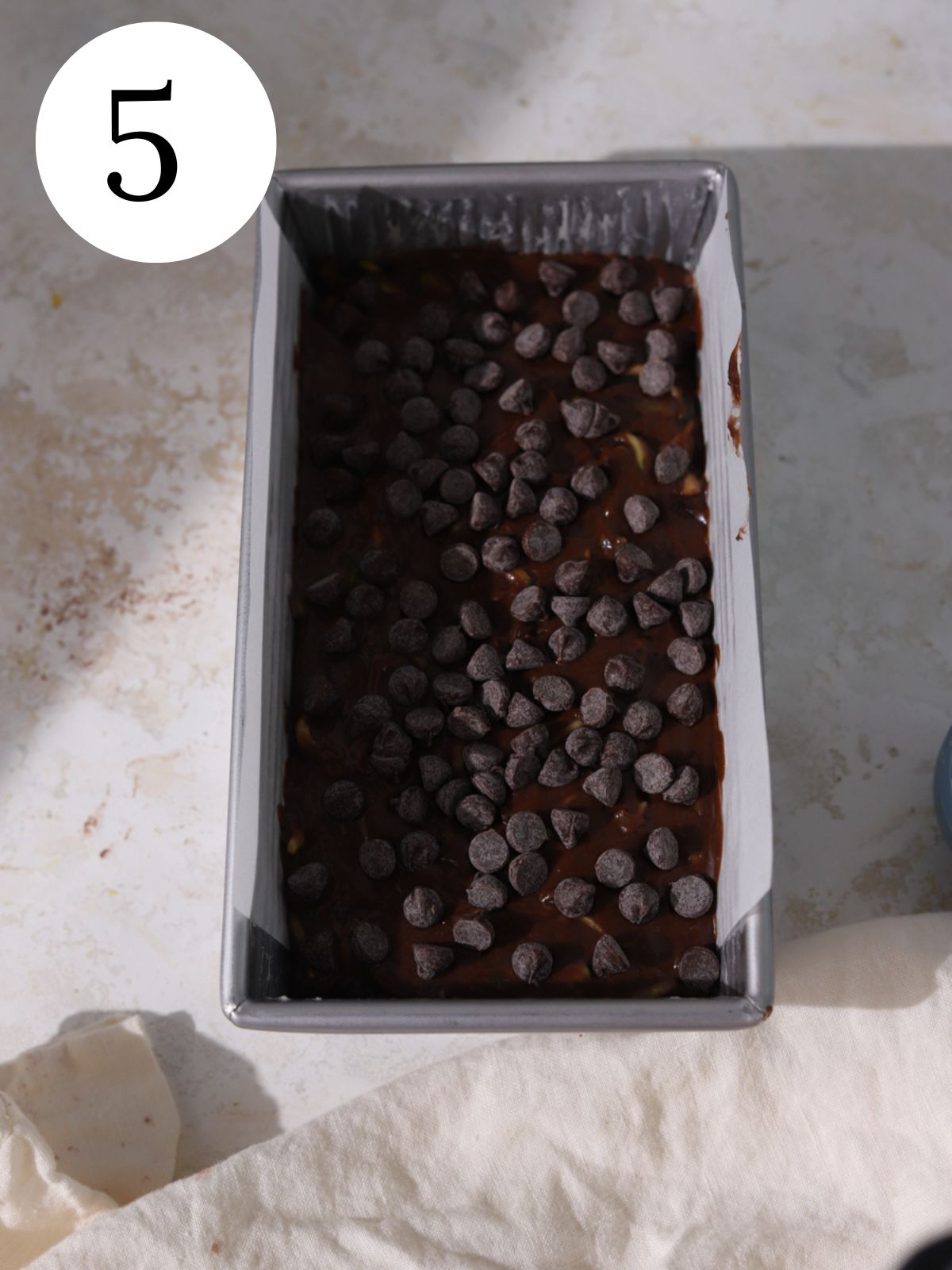 Chocolate zucchin bread batter in a loaf pan with chocolate chips on top.