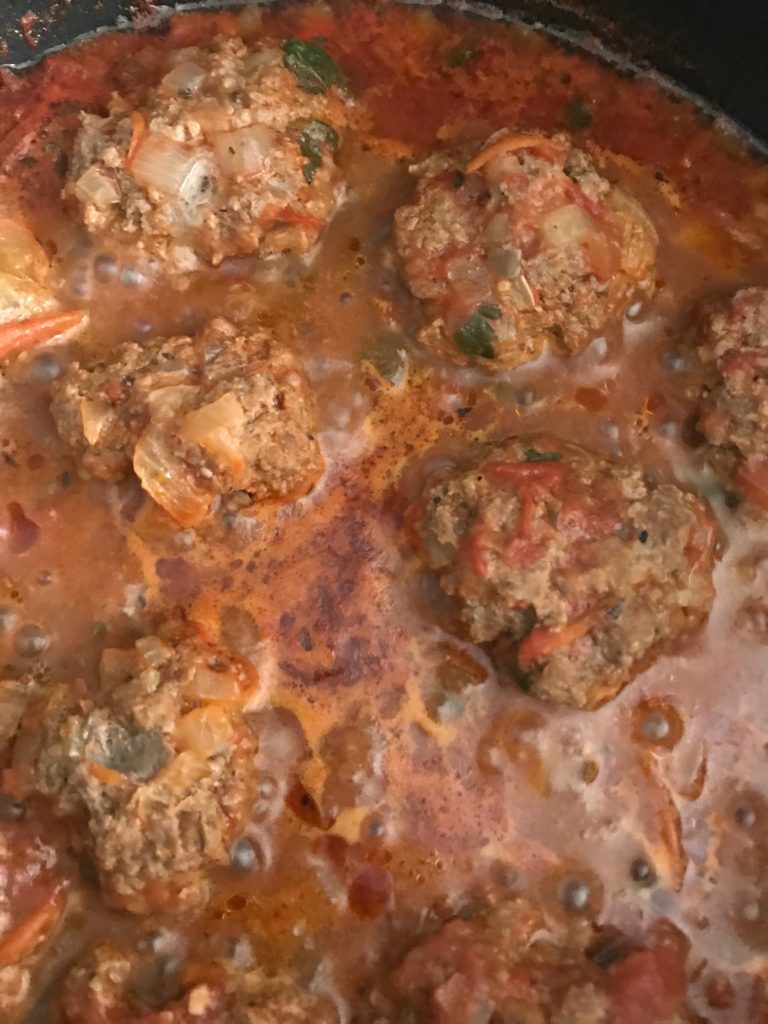 Succulent kofta meatballs cooking in simmering, thick tomato sauce. 