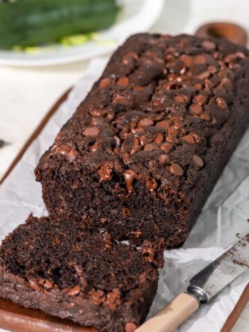 Chocolate zucchini bread being sliced with a knife next to it.