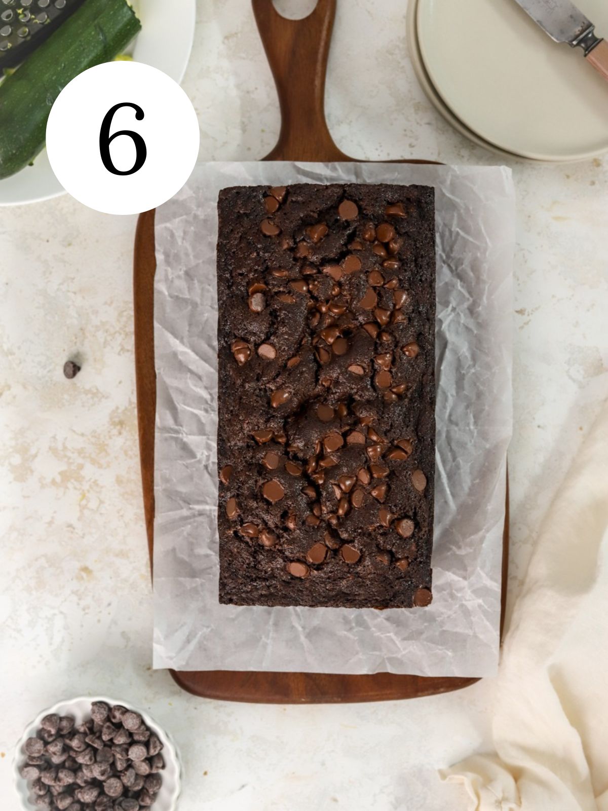 Double chocolate zucchini bread on parchement paper next to some plates.