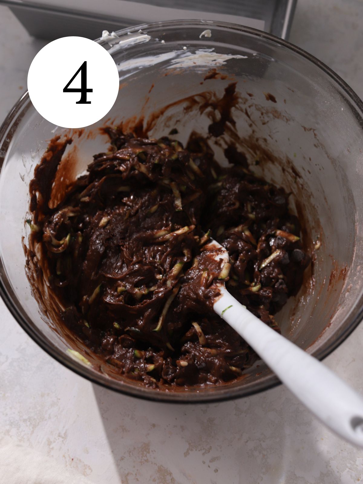 Zucchini in a bowl of chocolate bread batter with a spatula in it.