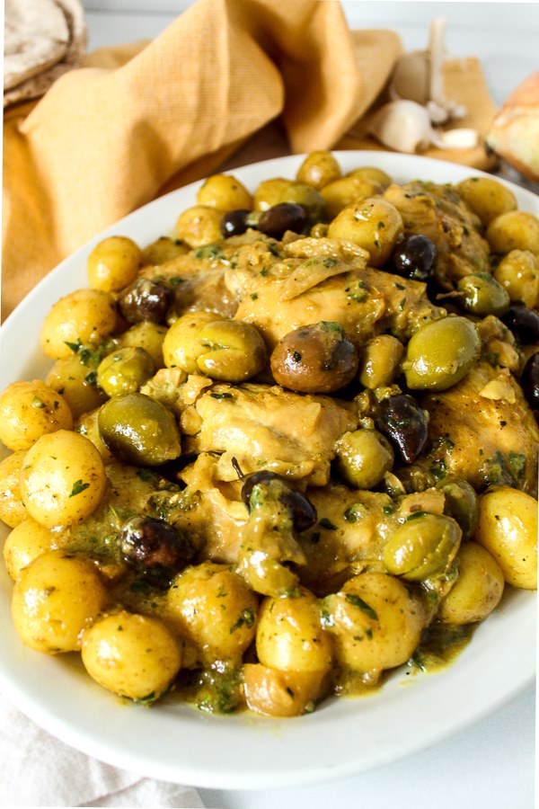 A platter with braised chicken, olives and herbs. 