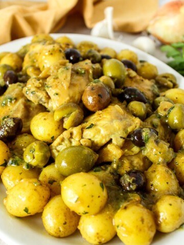 a large white platter with chicken thighs, potatoes, and olives
