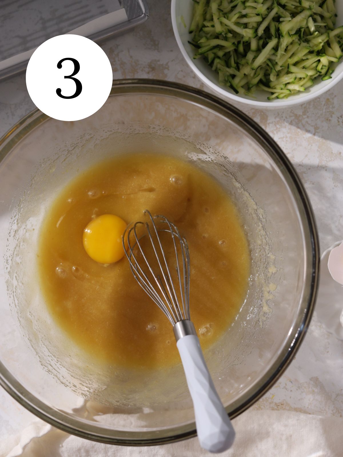 An egg added to a bowl of wet ingredients with a whisk.