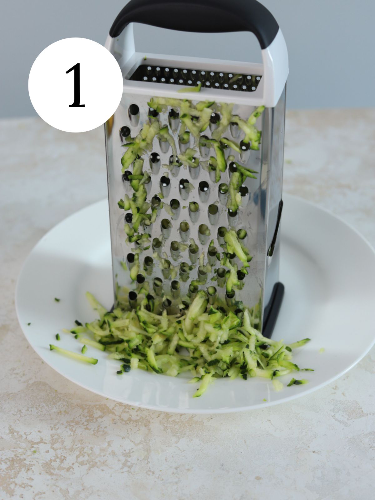 A box grater on a plate with shredded zucchini.