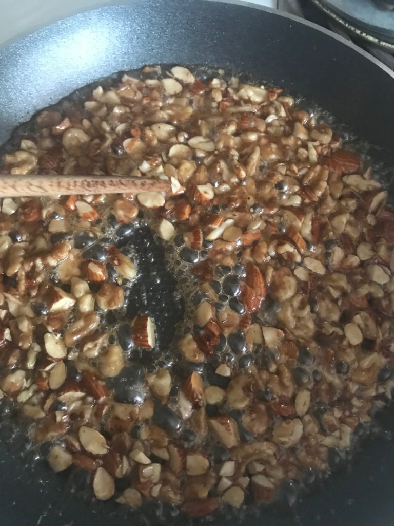 a pan with hot maple syrup cooking with chopped walnuts and a wooden spoon stirring them 