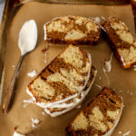 molasses marble cake slices with cream cheese frosting on browna parchment paper lined baking sheet with a spoon on it and two glasses of milk behind it