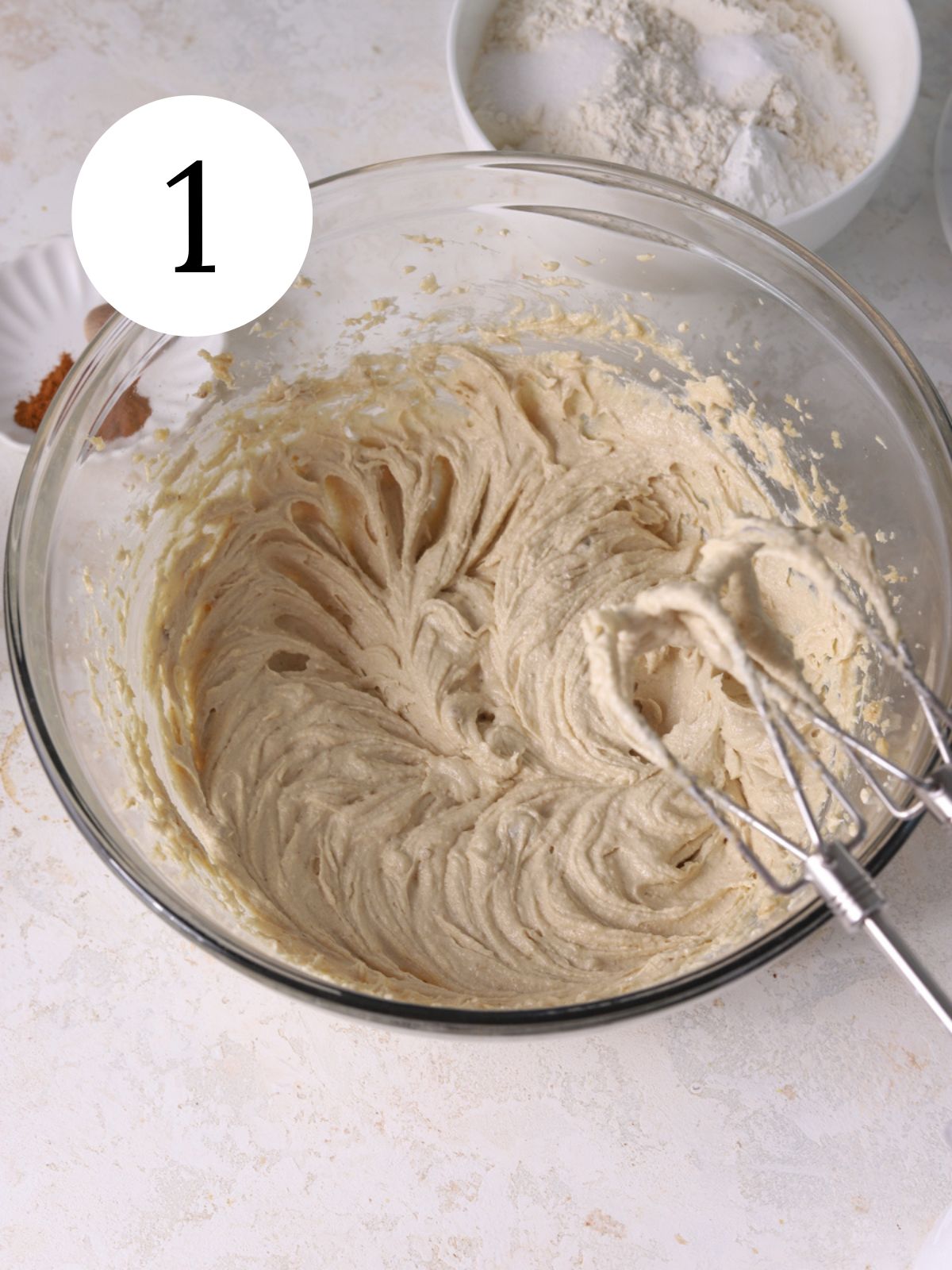 A glass bowl with sugars and butter being mixed with an electric mixer. 
