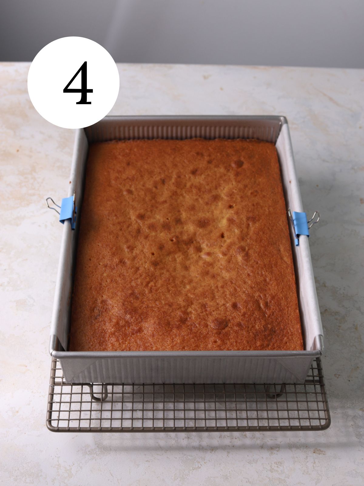 A wire rack with a rectangular cake in a pan set on it.