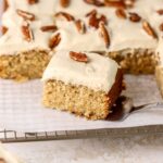 A piece of maple cake with frosting and pecans on a wire rack.