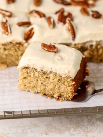 A piece of maple cake with frosting and pecans on a wire rack.