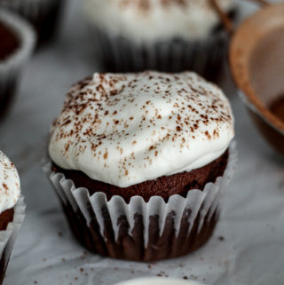 chocolate gingerbread cupcakes with whipped cream and cocoa on a counter with some molasses and cocoa on the counter