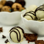 white chocolate covered truffle with chocolate chips next to it and white bowls filled with truffles behind it