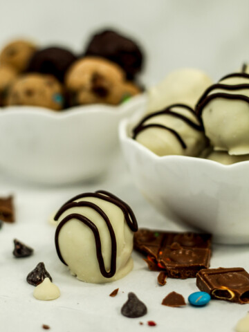 white chocolate covered truffle with chocolate chips next to it and white bowls filled with truffles behind it