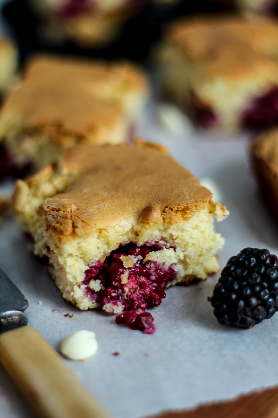 A freshly baked piece of white chocolate cake with a baked blackberry oozing out.