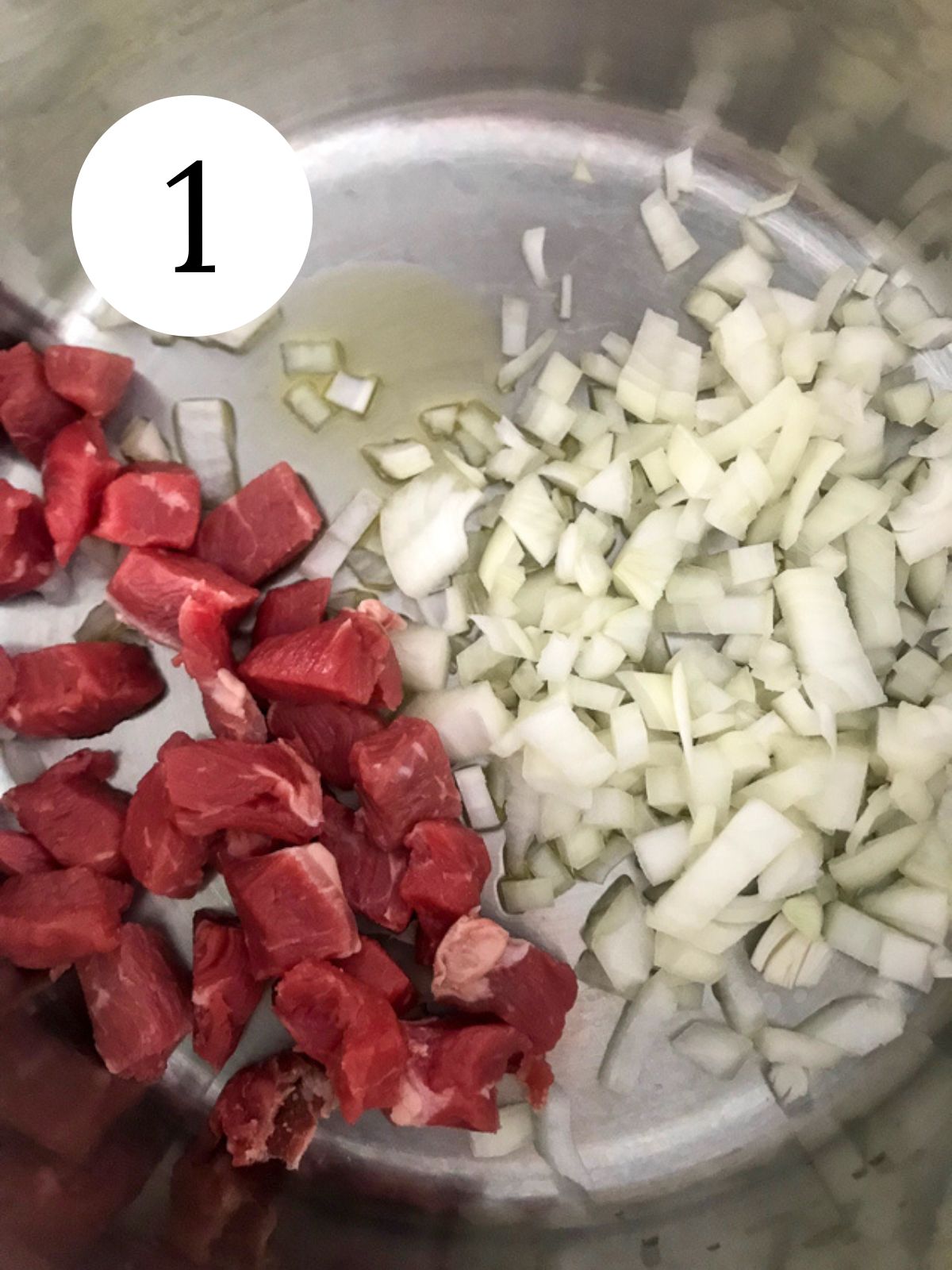 Cubed beef and chopped onions in a pot with some olive oil.