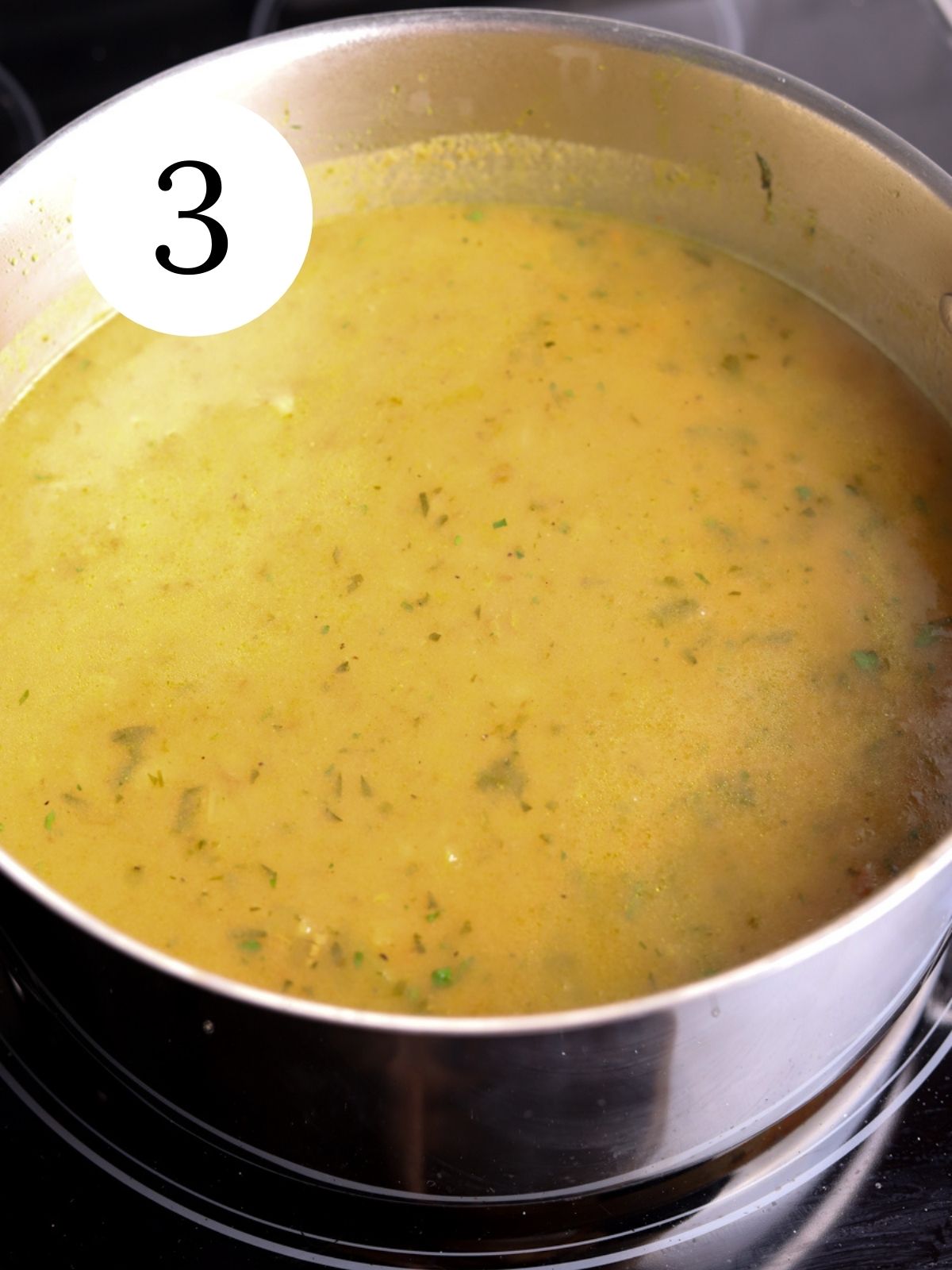 Tomatoes and herbs added to a large pot of soup on the stovetop.