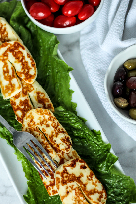 Freshly fried halloumi  slices arranged on a bed of lettuce next to a red cabbage salad.