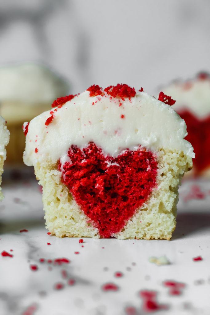 Half of a cupcake with red velvet hearts inside topped with vanilla buttercream.