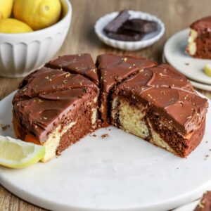 Single layer marbled cake with chocolate frosting on a platter with a slice of lemon.