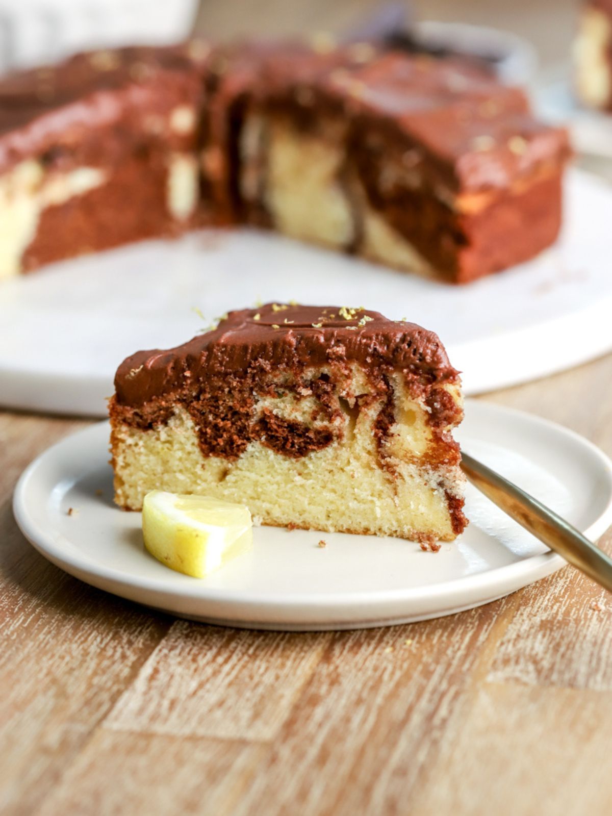 A slice of lemon and chocolate marbled cake on a plate with a lemon slice.