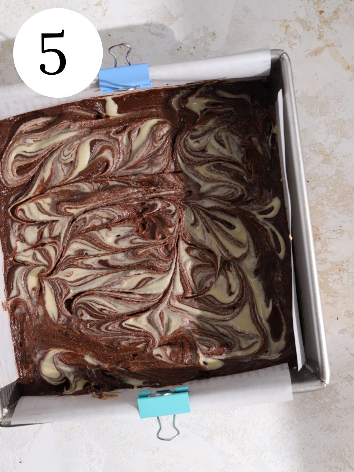 Brownie batter in a pan with tahini swirled in it. 