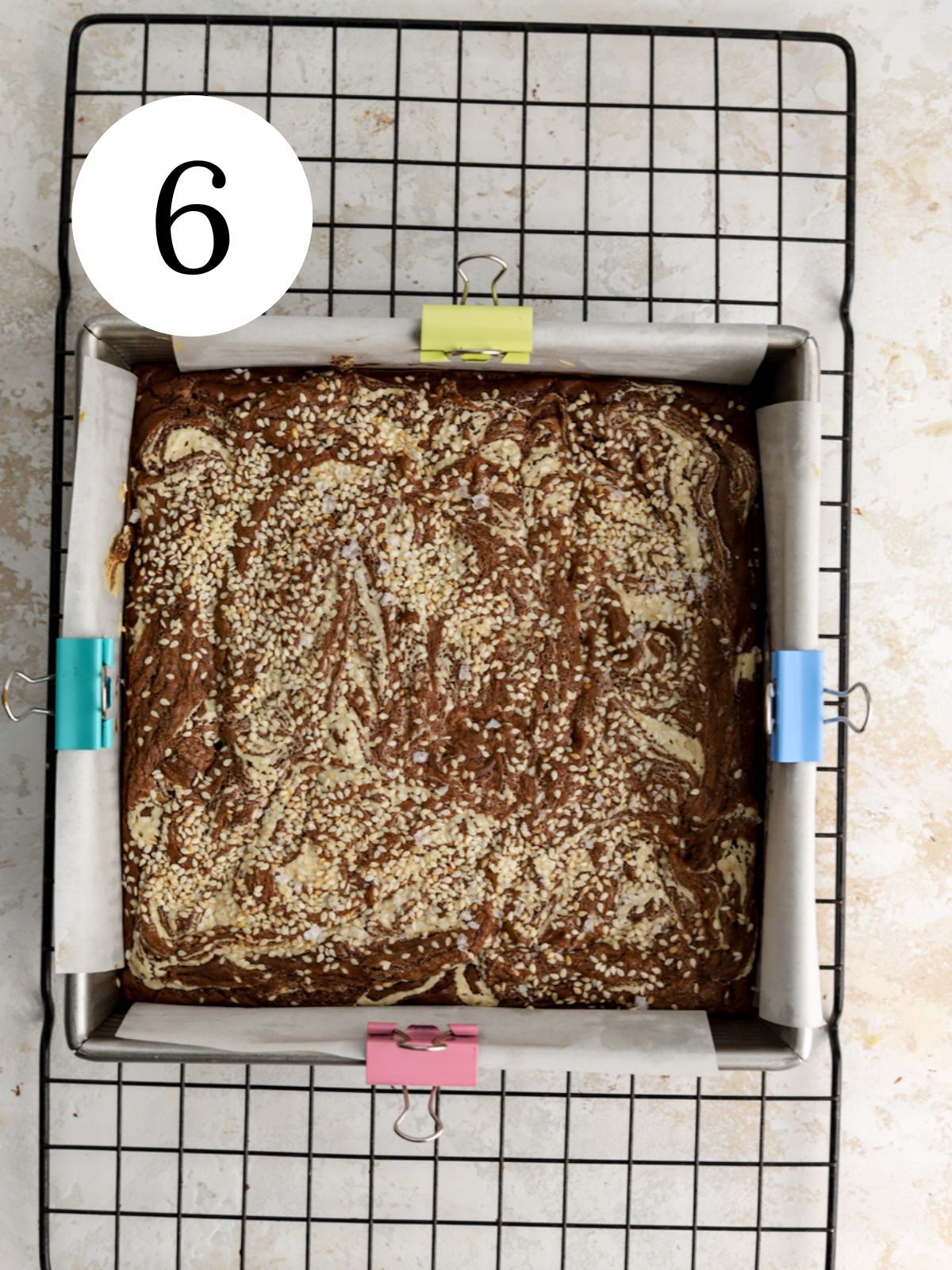 A pan of brownies with tahini and sesame seeds on a cooling rack. 