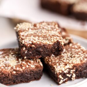 Tahini brownies with sesame seeds stacked on a plate.