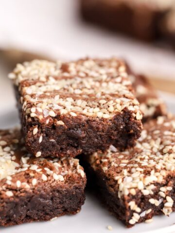 Tahini brownies with sesame seeds stacked on a plate.