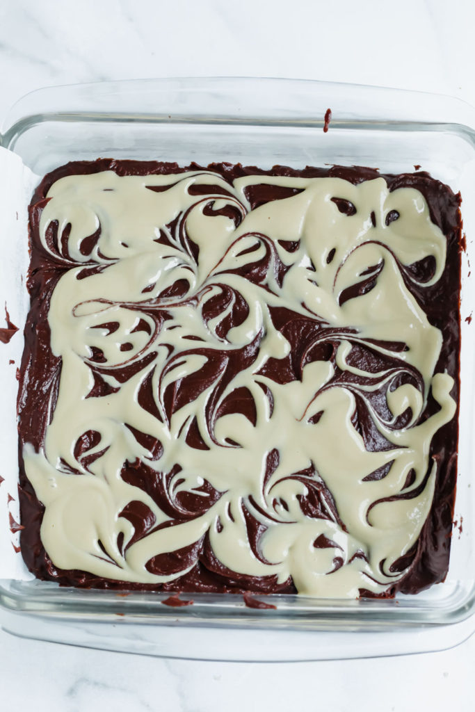 Fudgy chocolatey brownie batter in a pan with tahini drizzled and swirled on top. 