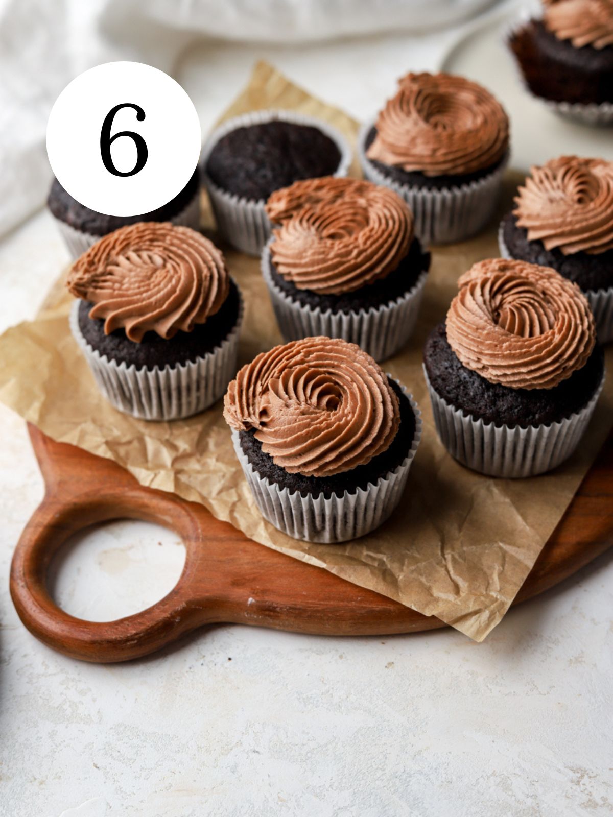 A batch of chocolate cupcakes with chocolate frosting on parchment paper.