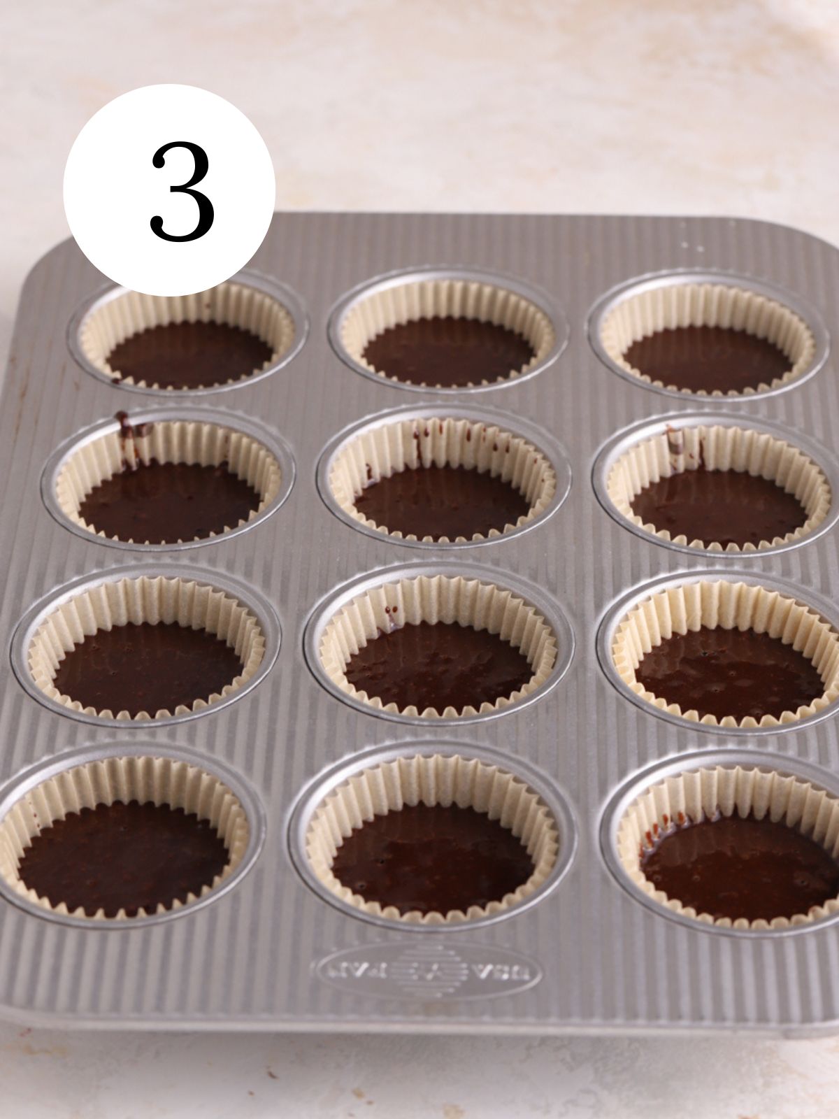A cupcake pan filled halfway with chocolate cupcake batter.