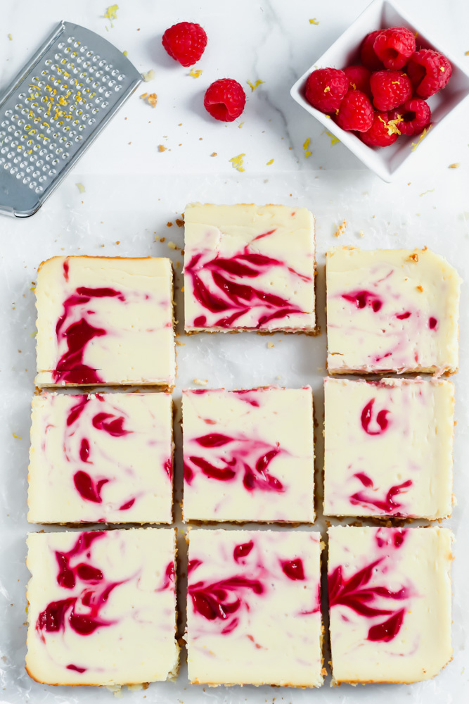 A batch of cheesecake bars cut into squares with raspberry swirled in them. 
