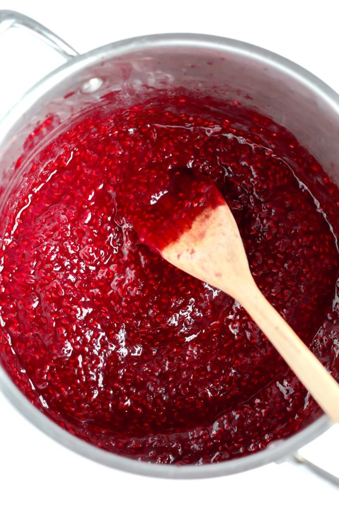Raspberry sauce in a pot with a wooden spoon in it. 
