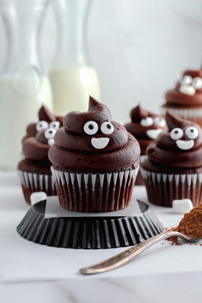 Rich chocolate buttercream frosting piped in a poop shaped swirl on top of chocolate cupcakes. 