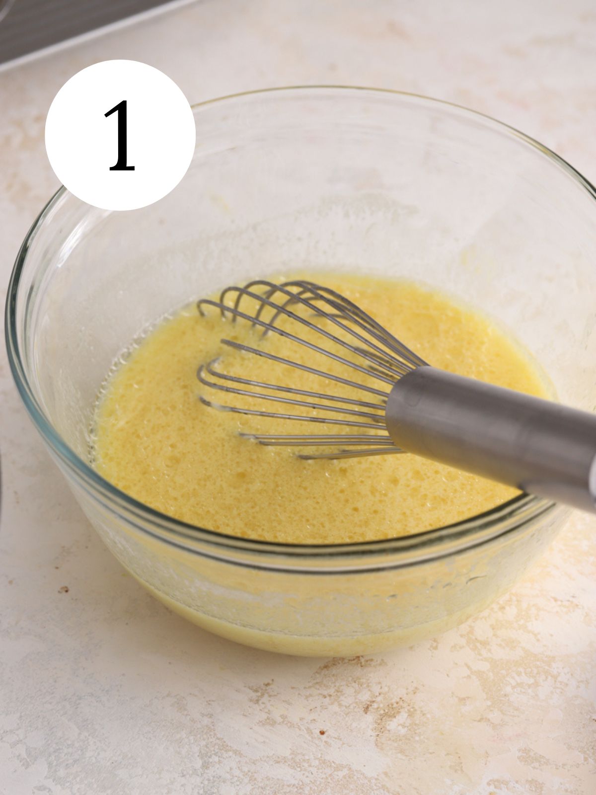 A glass mixing bowl with wet ingredients being whisked together.