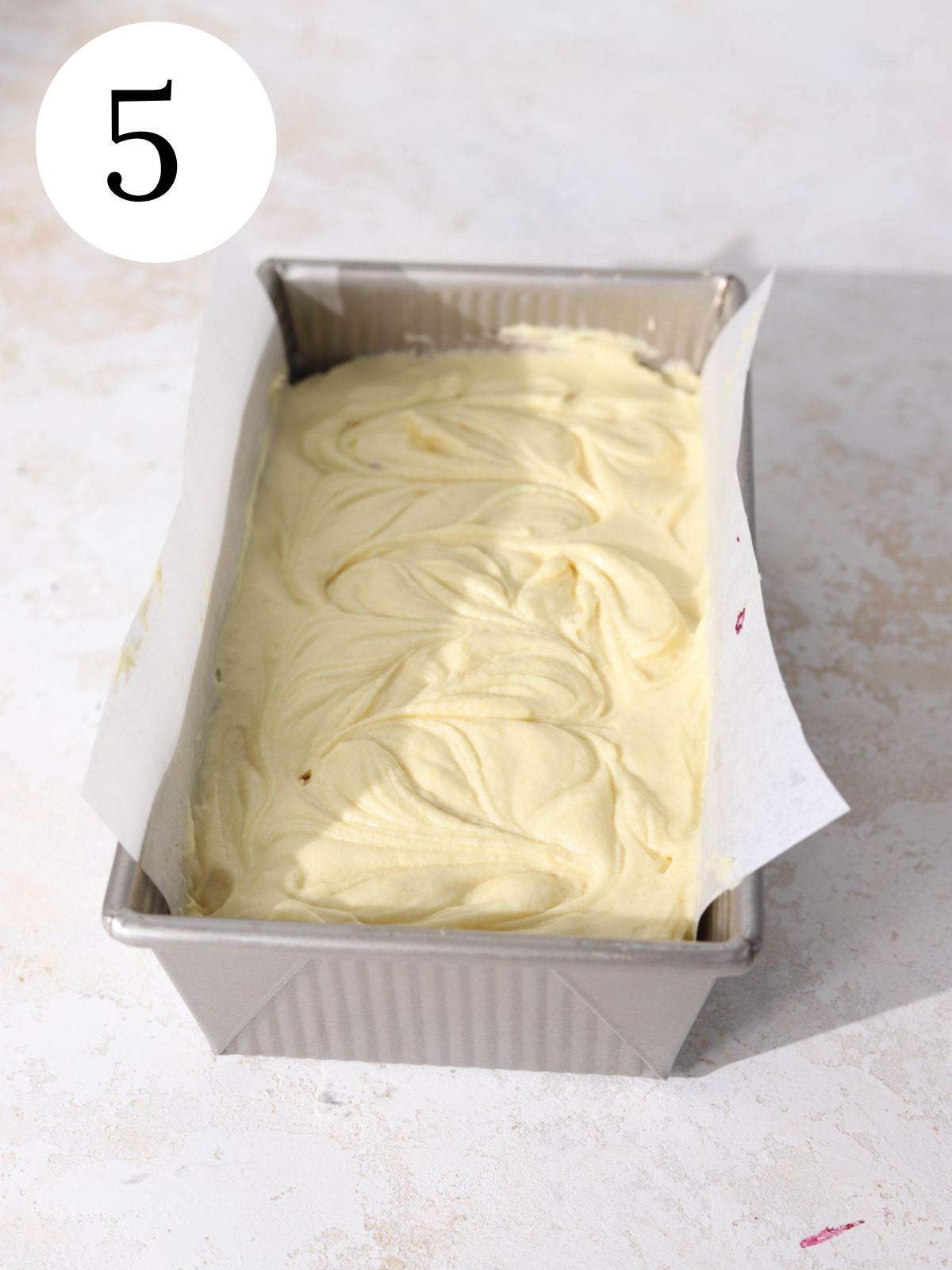A loaf pan lined with parchment paper filled with cake batter.