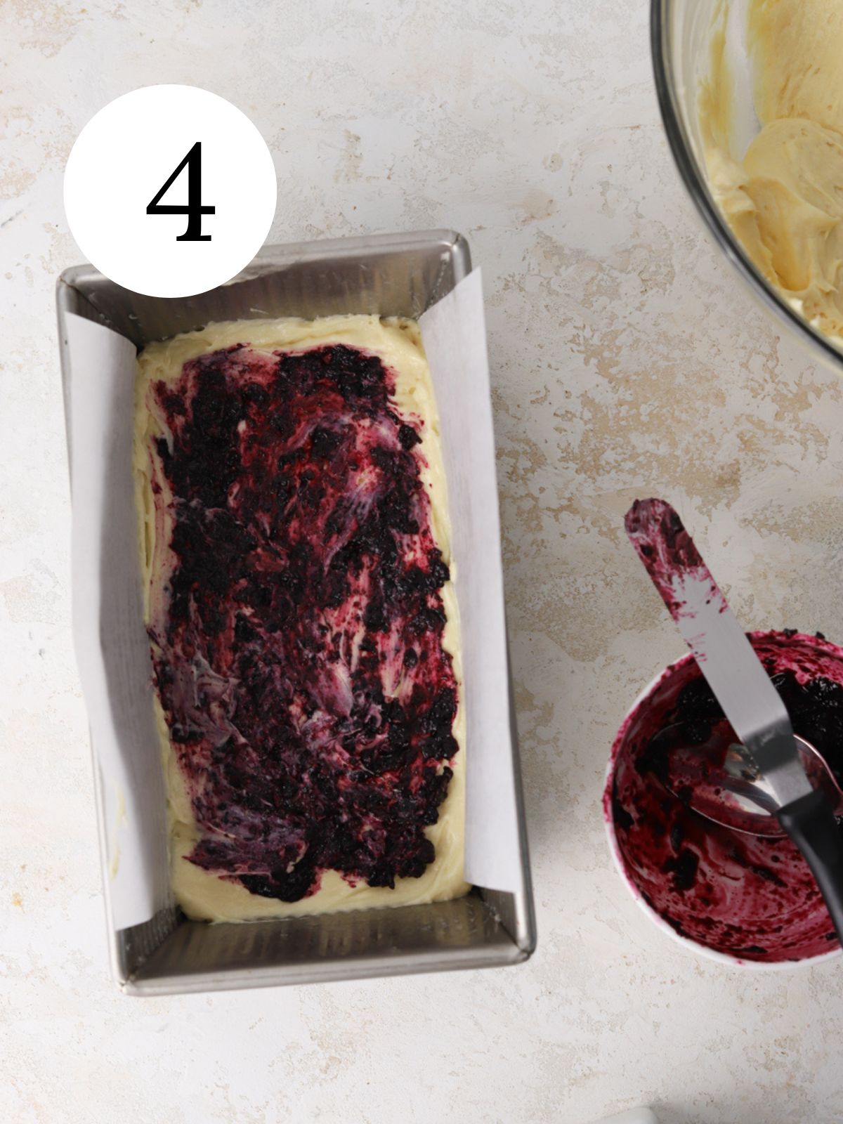 A loaf pan with batter and jam spread on top.