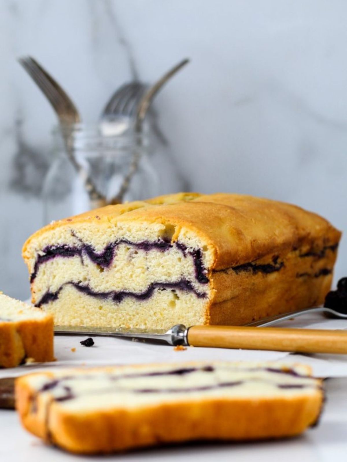A pound cake sliced open with blueberry jam swirled inside next to a knife.
