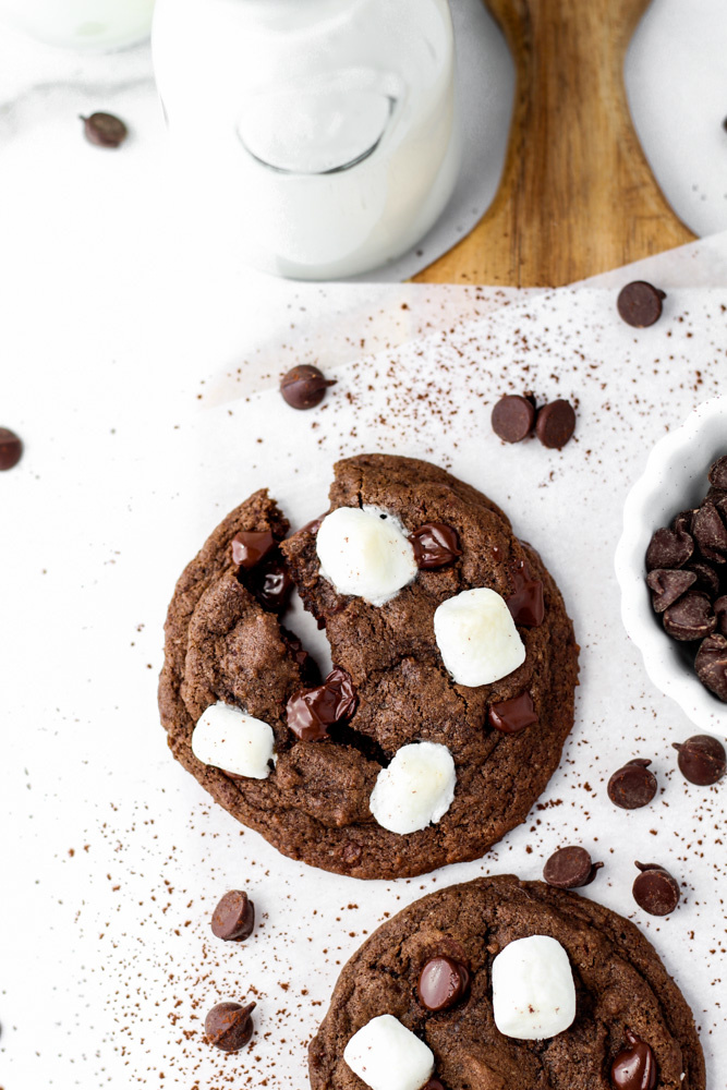 cookies made with cocoa, chocolate chips and mini marshmallows next to a jug of milk.