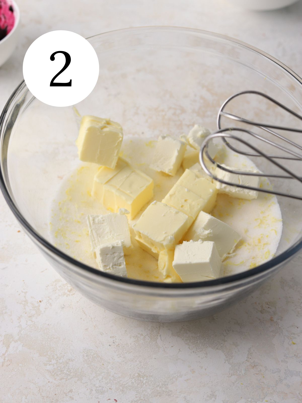 A large mixing bowl with lemon sugar, chopped butter and cream cheese.