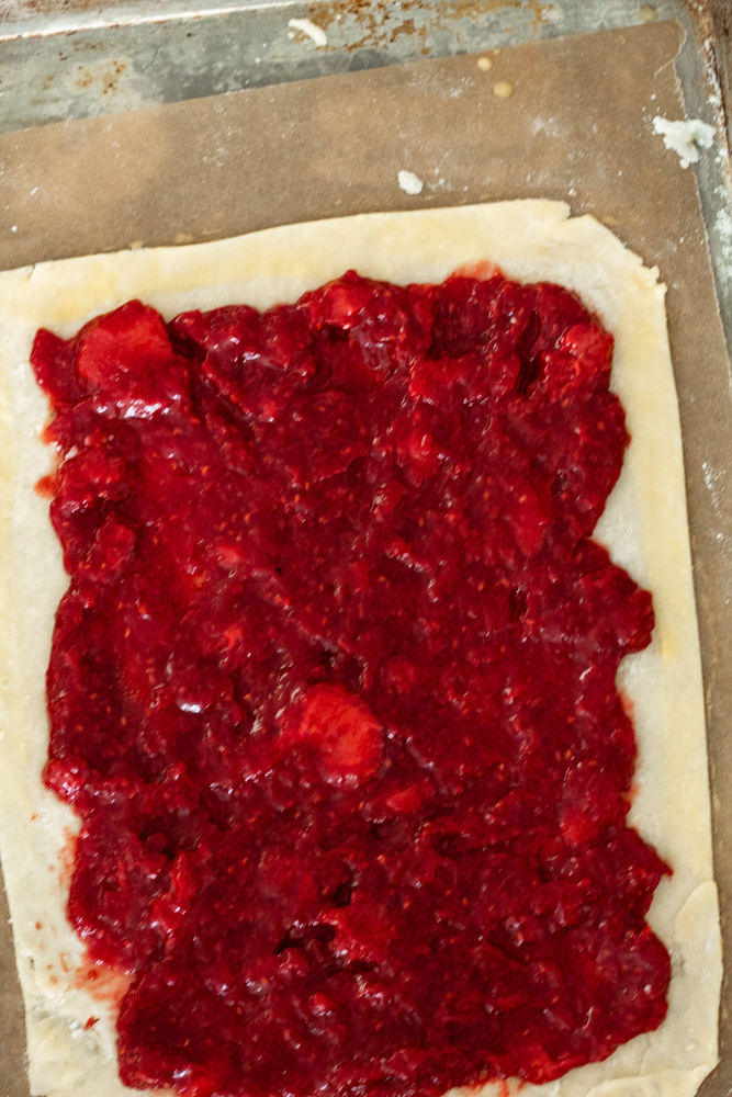 Pie crust rolled out in a rectangle covered with bright red strawberry jam. 